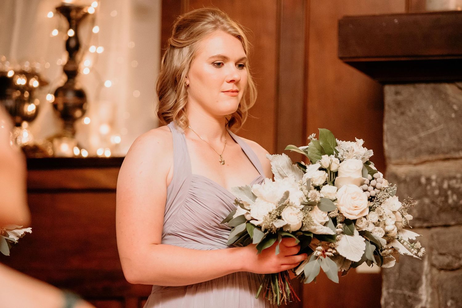 Bridesmaid in gray dress holding white rose bouquet with eucalyptus at elegant wedding ceremony.
