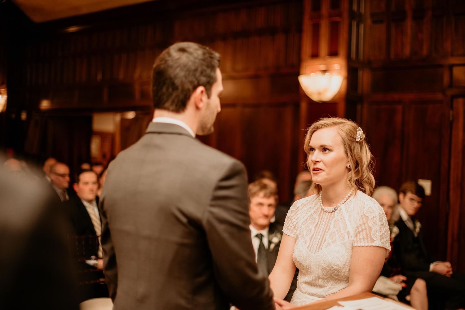 Bride and groom exchange vows during an intimate wedding ceremony in an elegant wood-paneled venue.