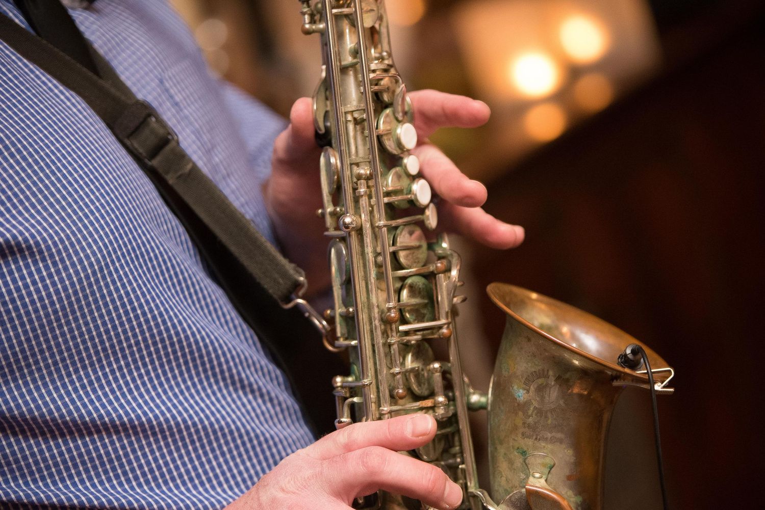 Close-up of a musician playing a brass saxophone, fingers on keys, with warm bokeh lights in the background.