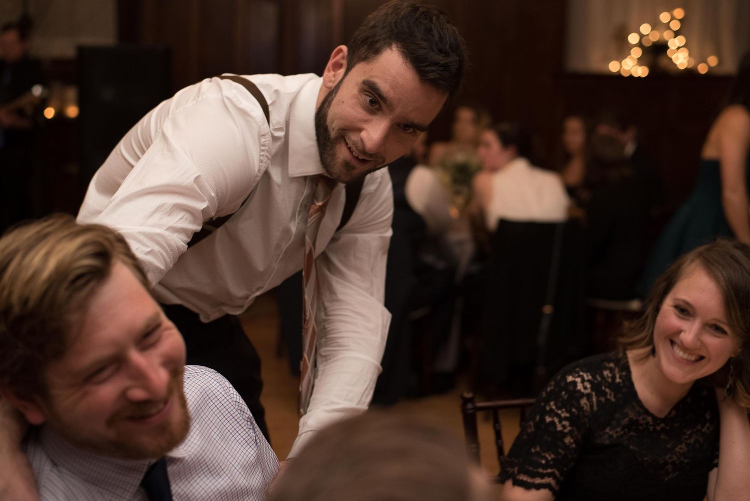 Man in white shirt and tie leaning over to chat with guests at a formal wedding reception dinner.