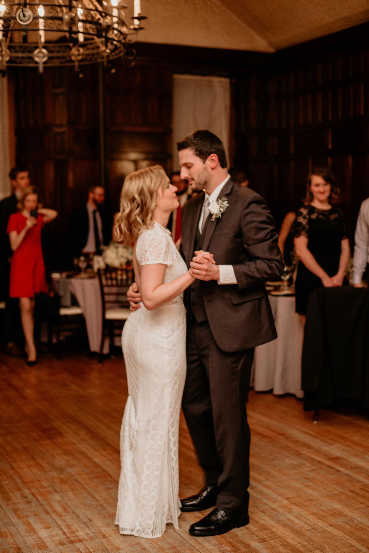 Bride and groom share their first dance at elegant wedding reception with guests watching in background.