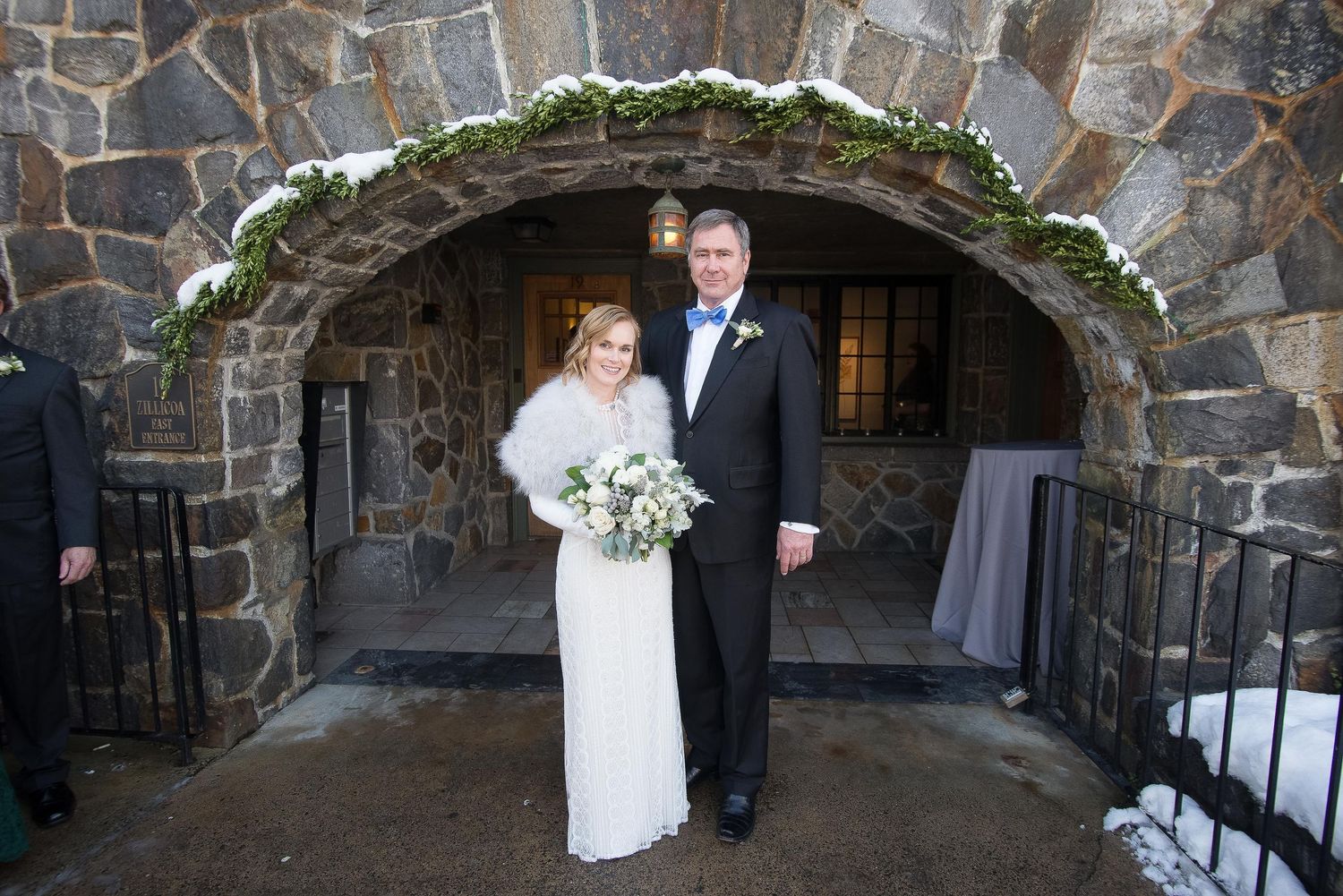 Bride and groom posing under a snow-dusted stone arch at a winter wedding venue.