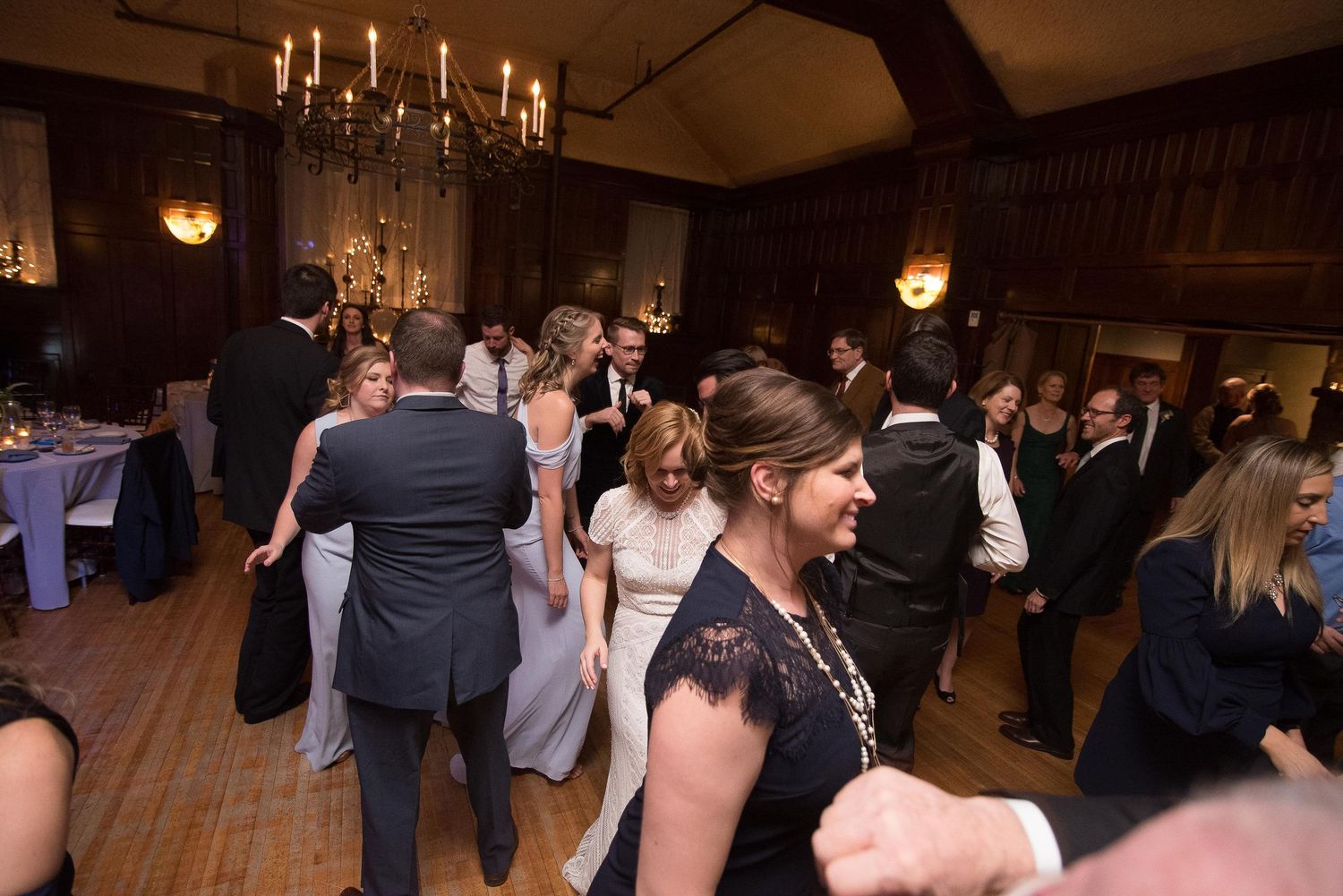 Guests dancing and celebrating at an elegant wedding reception in a warmly lit ballroom with chandeliers.