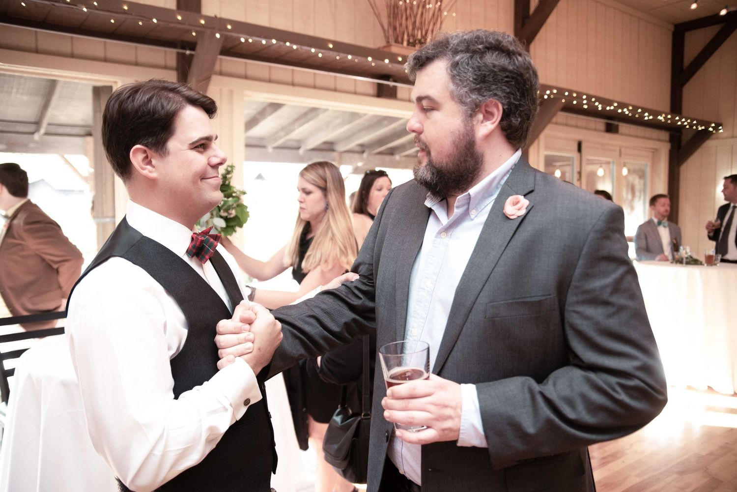 Two men in formal attire shaking hands and conversing at an elegant wedding reception venue.