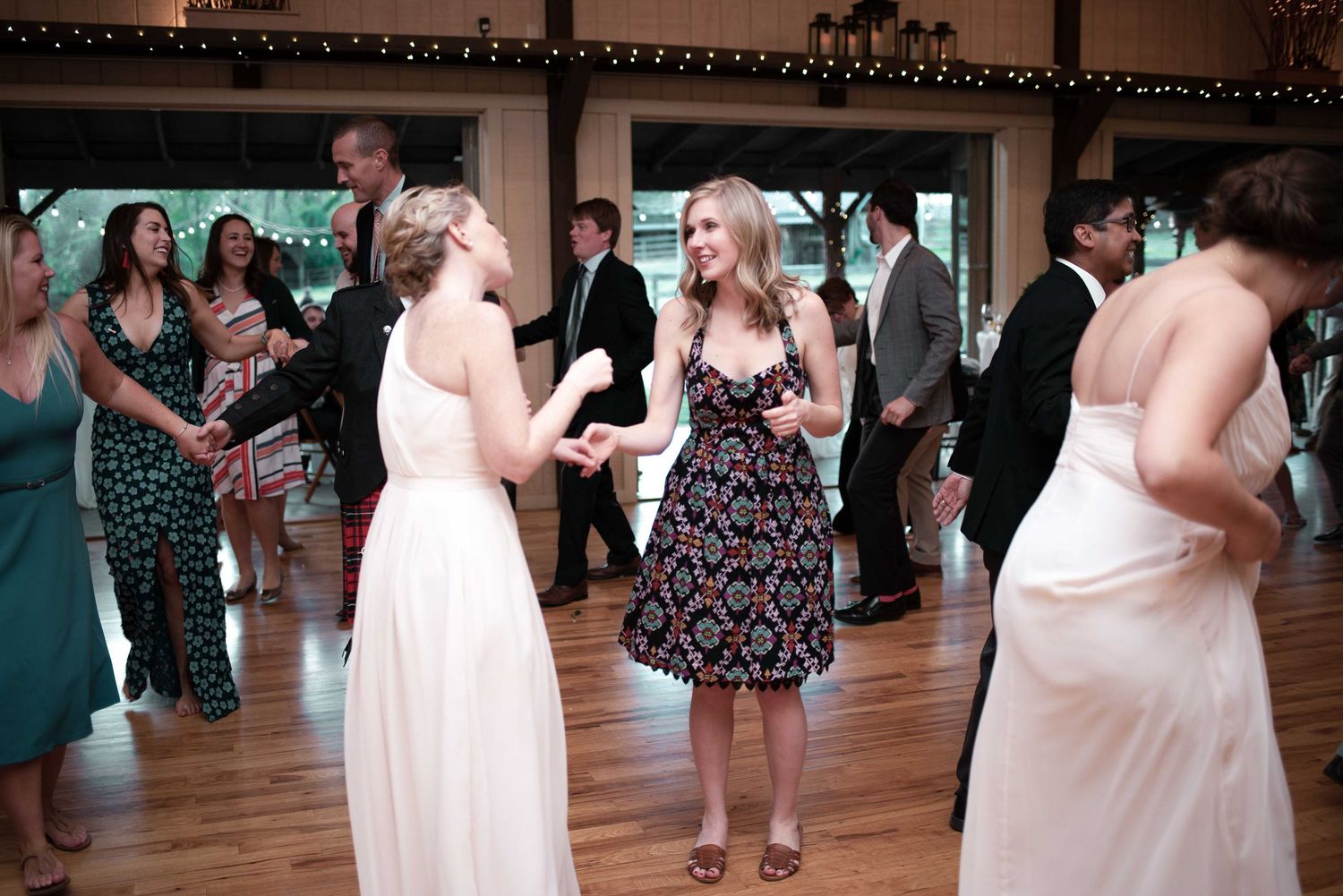 Guests dancing and socializing at a wedding reception on a wooden dance floor in an elegant venue.