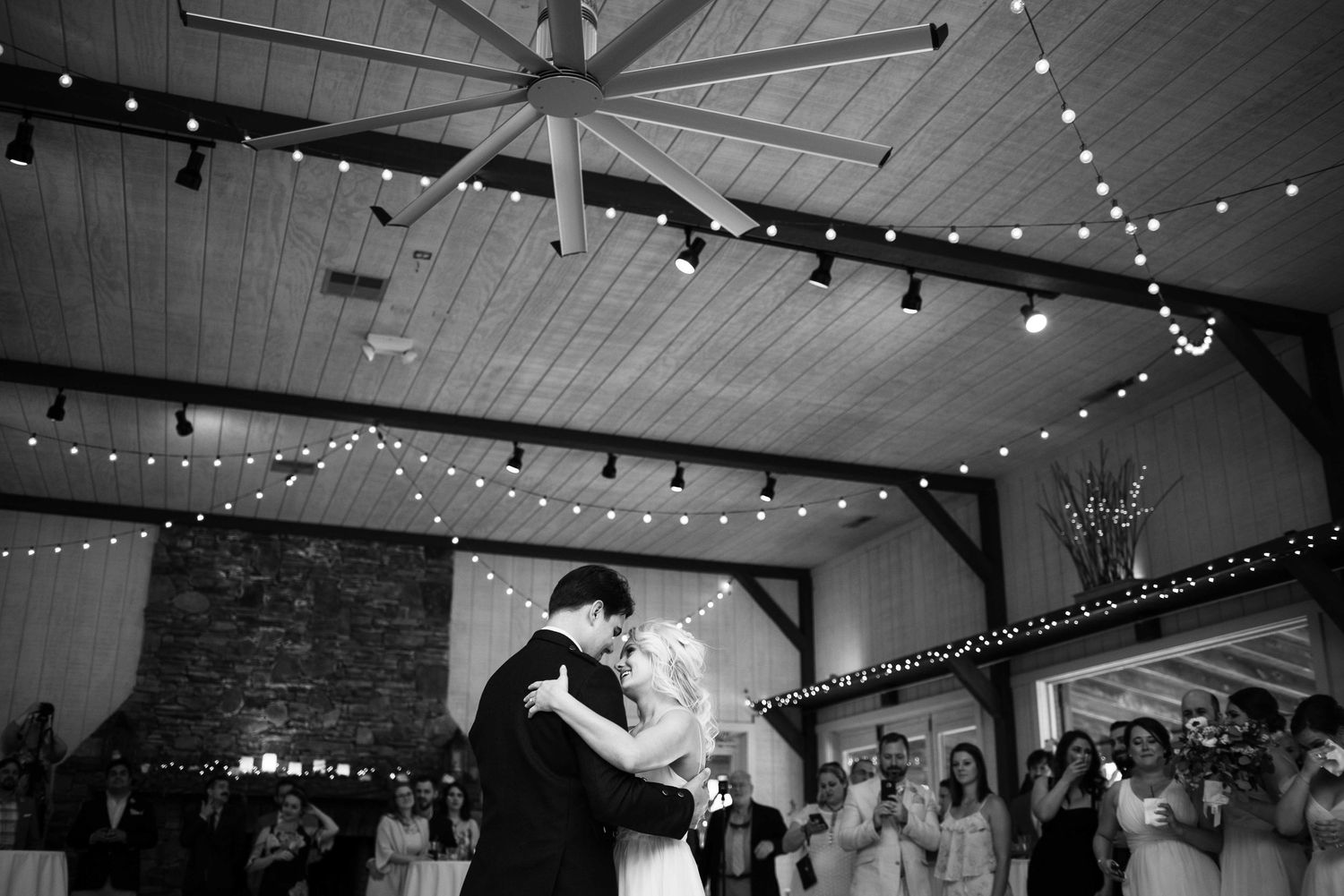 Bride and groom share first dance under string lights in elegant barn wedding venue.