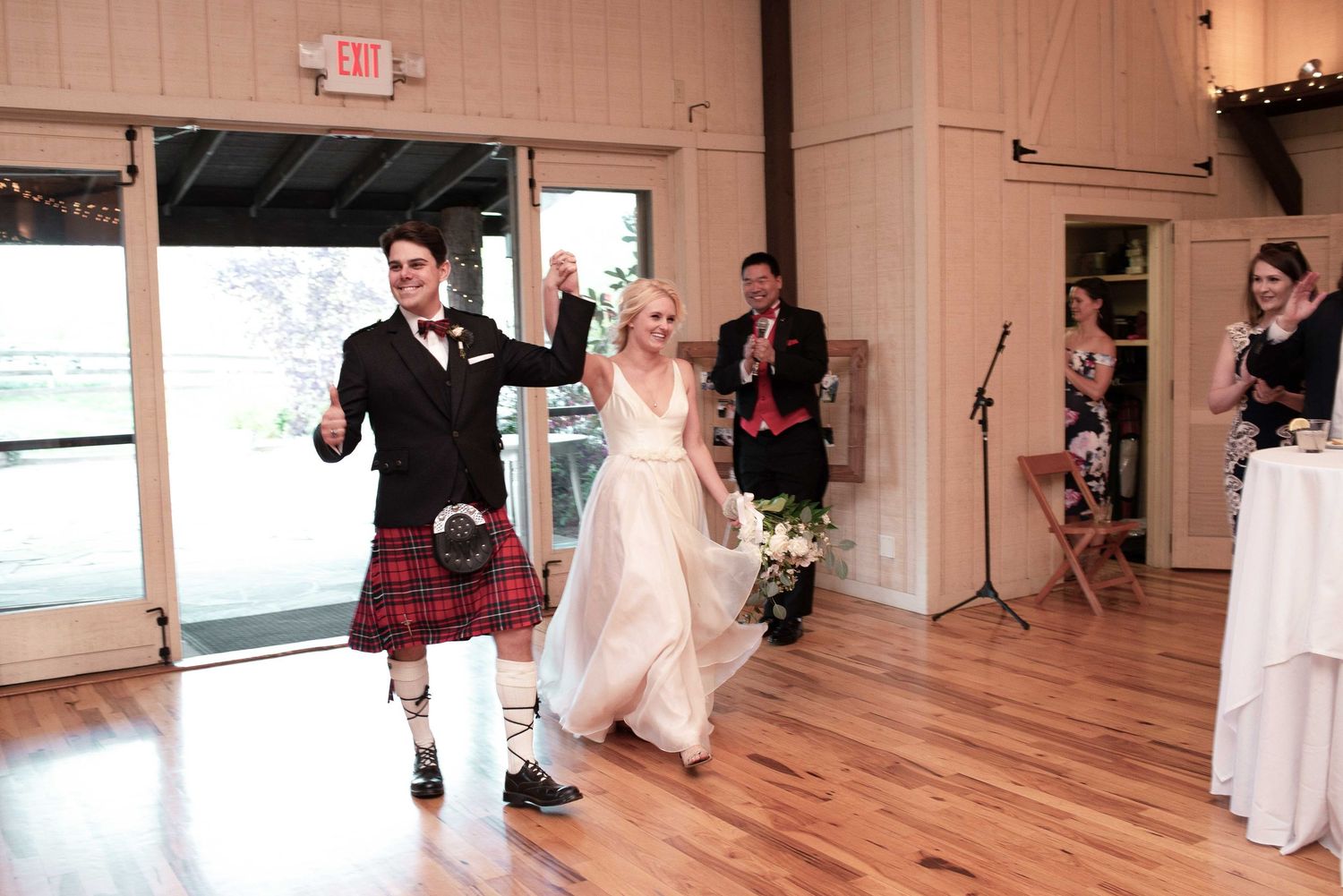 Bride and groom in Scottish kilt making grand entrance at wedding reception on hardwood dance floor.