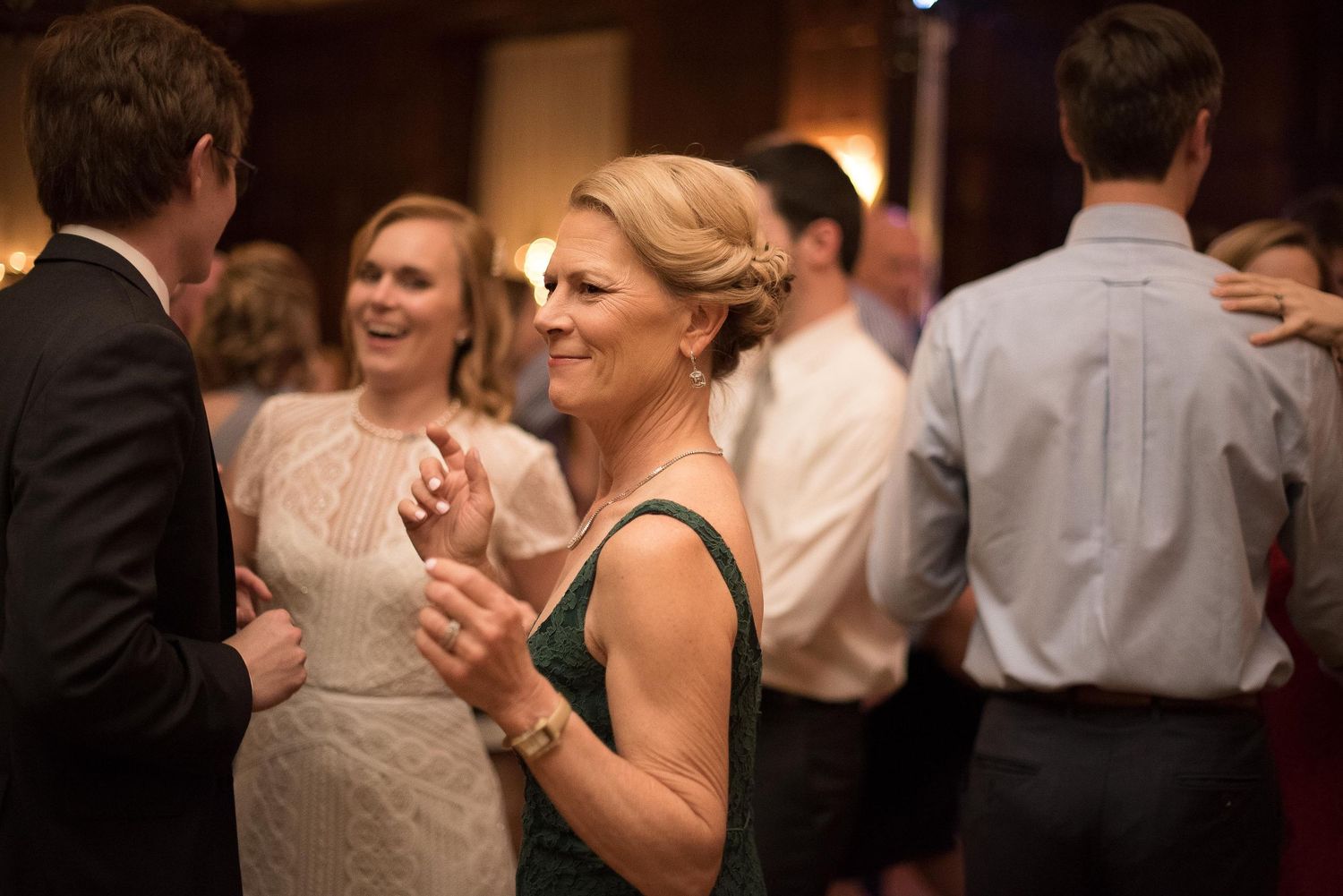 Elegant woman in green dress smiling and dancing at a formal event with guests in background.