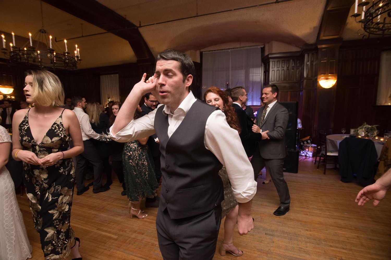 Guests dancing energetically at an elegant wedding reception in a grand ballroom with chandeliers.