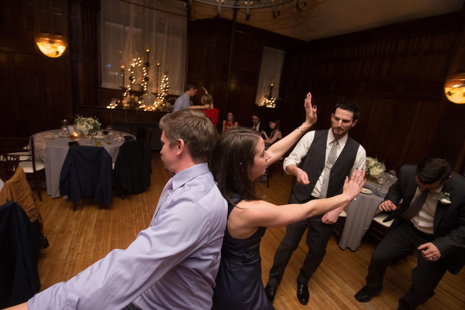 Guests dancing and high-fiving at a wedding reception in an elegant ballroom with decorated tables.