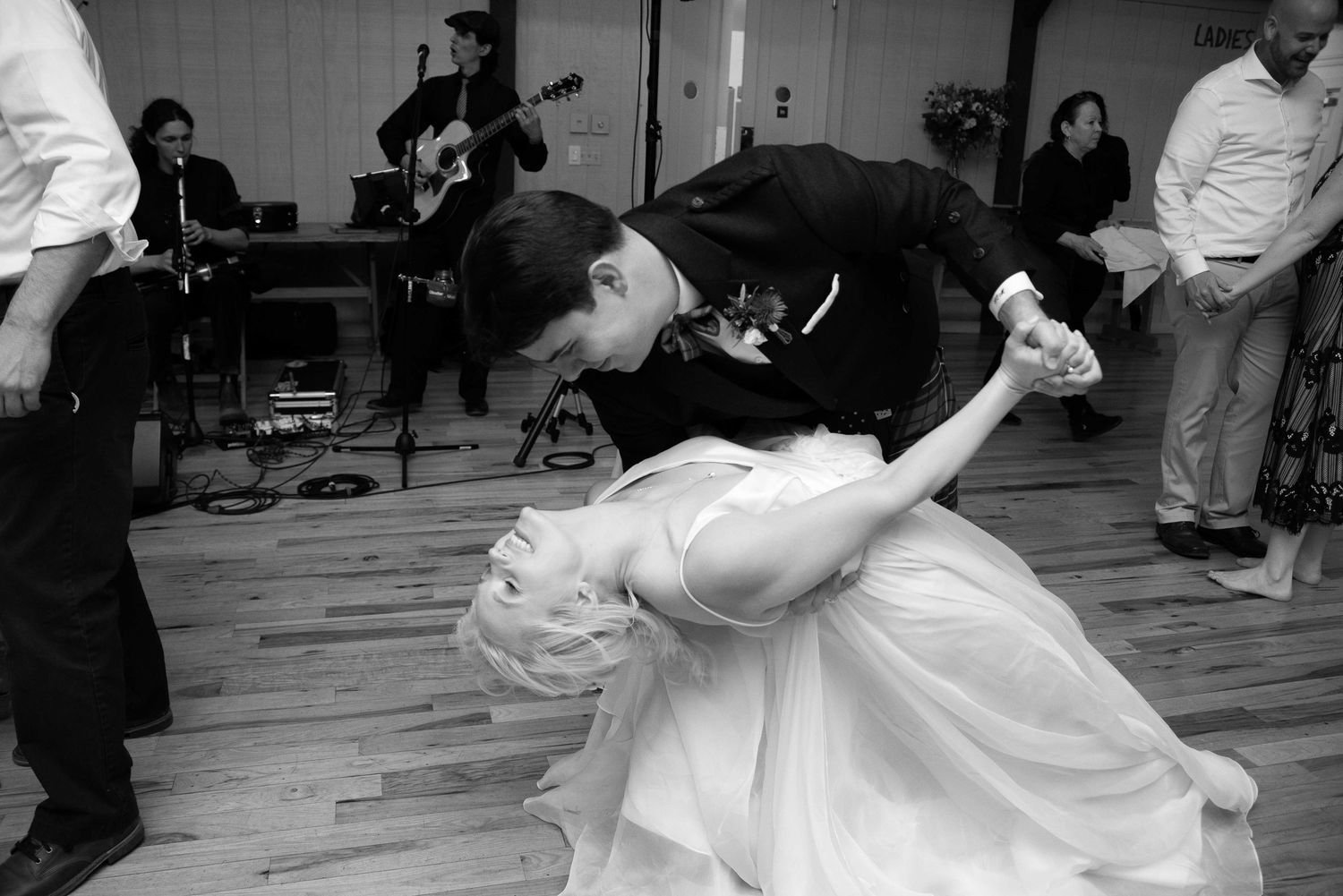 Black and white photo of a couple sharing a romantic dip dance at their wedding reception with a live band performing.