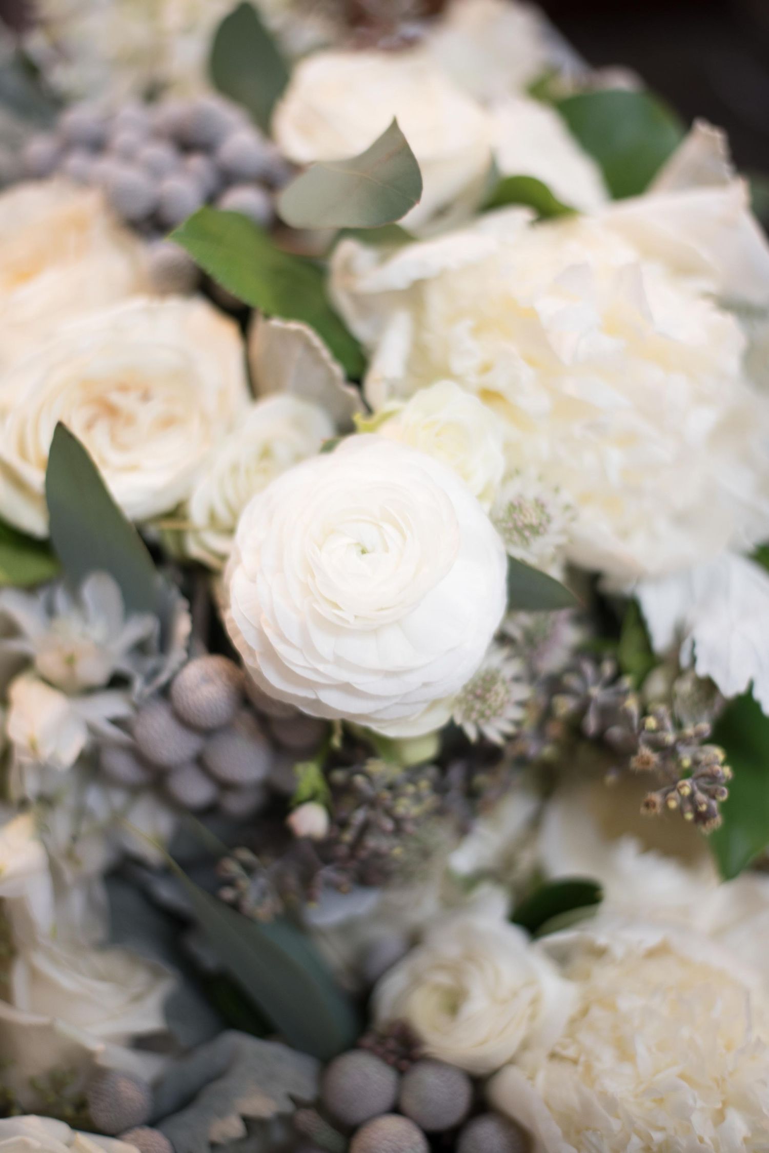 Elegant white ranunculus and roses with gray berries and eucalyptus in a soft, romantic floral arrangement.