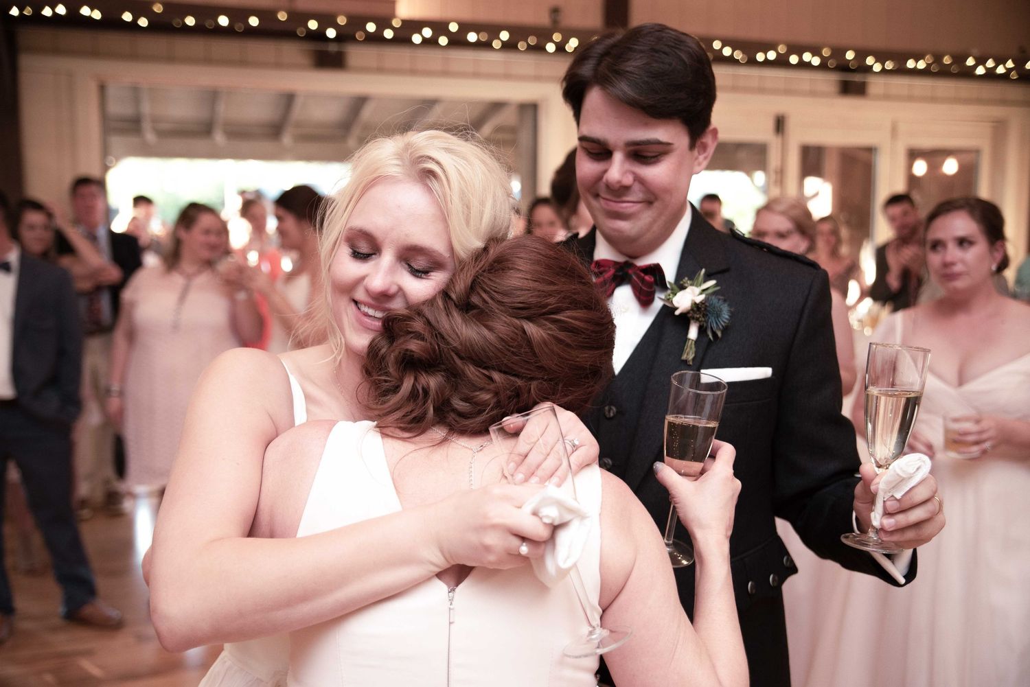 Bride and groom sharing emotional hugs with guests during wedding reception celebration.