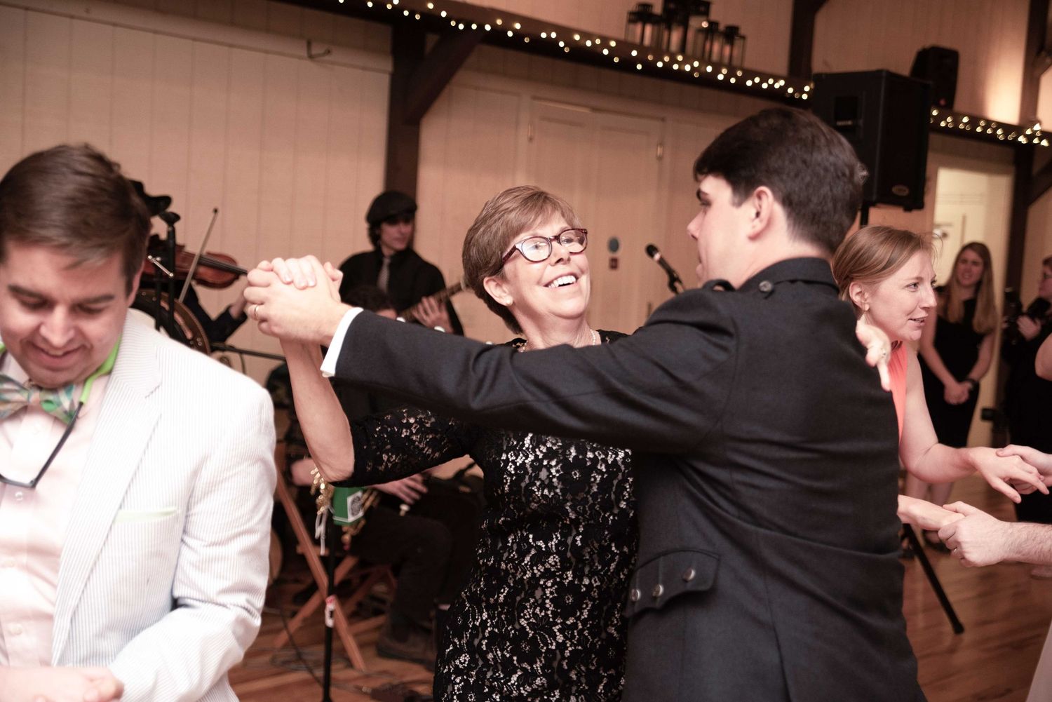 Guests dancing joyfully at a wedding reception in an elegant venue with string lights and a live band.
