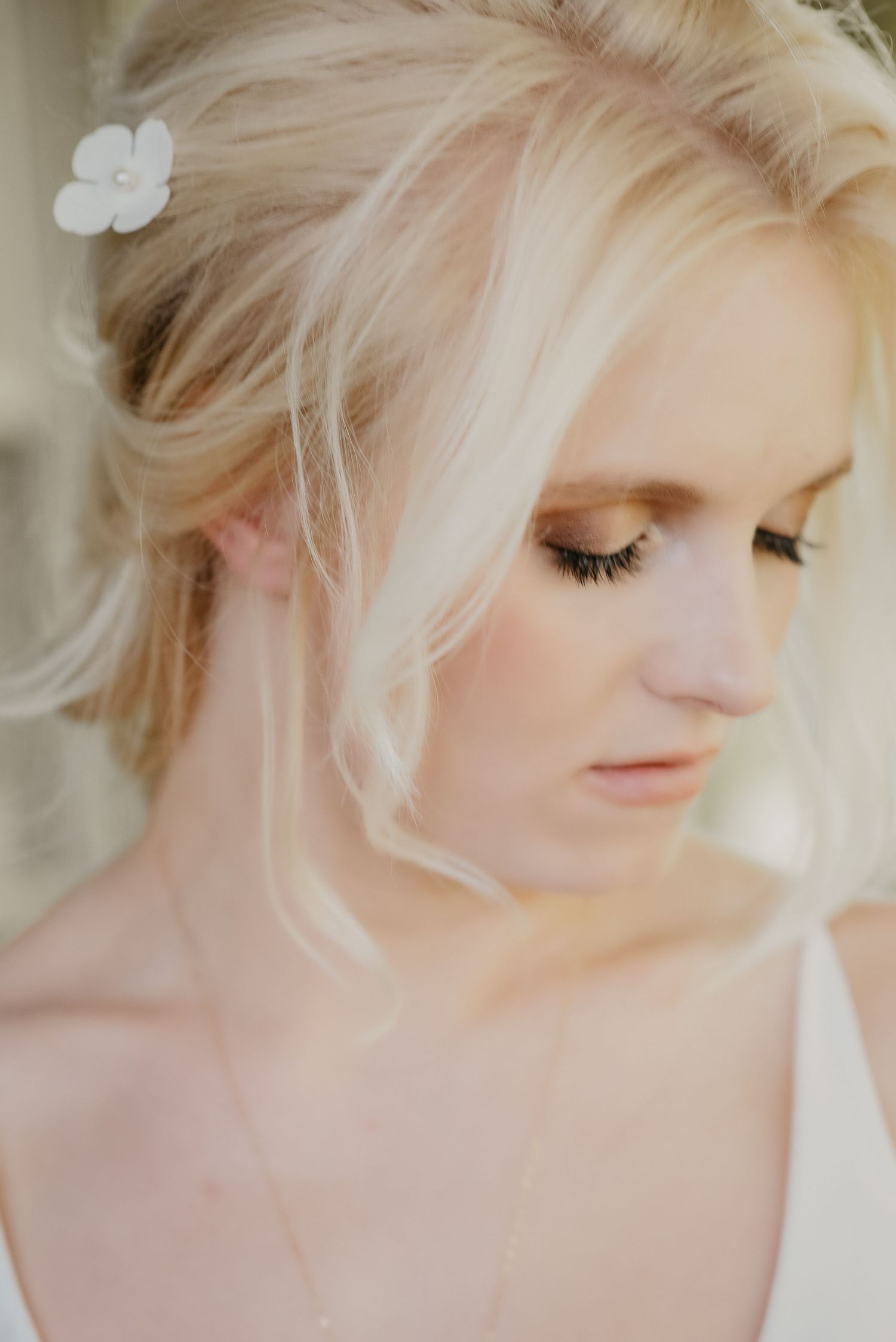 Close-up portrait of a blonde bride with soft updo hairstyle adorned with a white flower hair accessory.