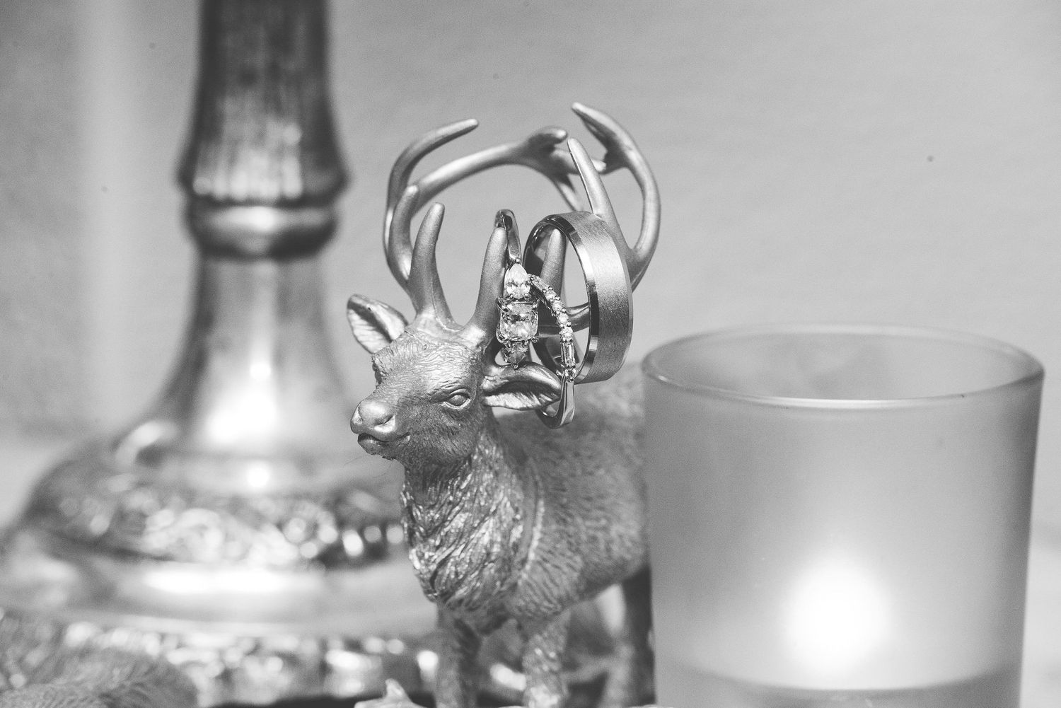 Silver deer figurine with antlers beside a lit frosted glass candle and ornate candlestick in monochrome.