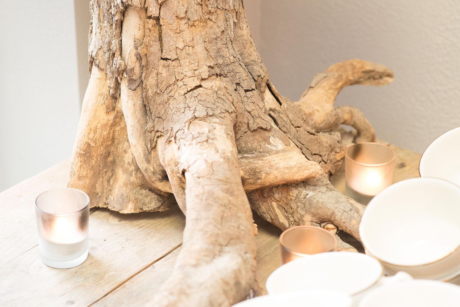 Rustic driftwood centerpiece with white bowls and candles on a wooden table.