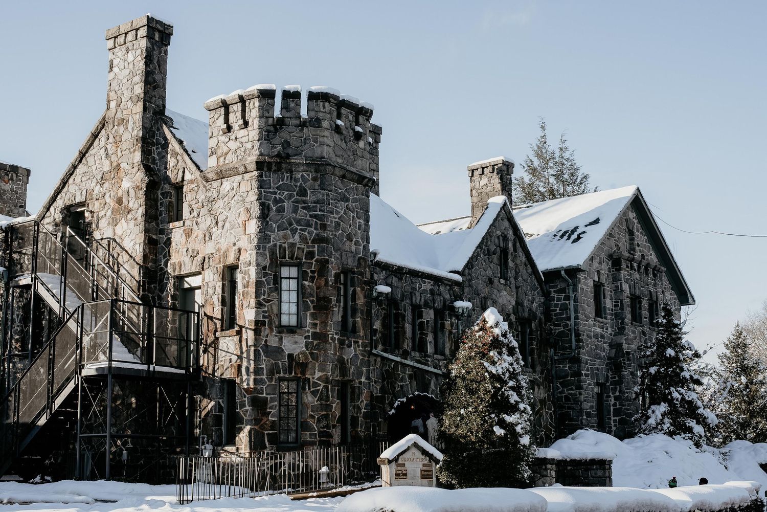 Snow-covered stone castle with turrets and chimneys under a clear blue winter sky.