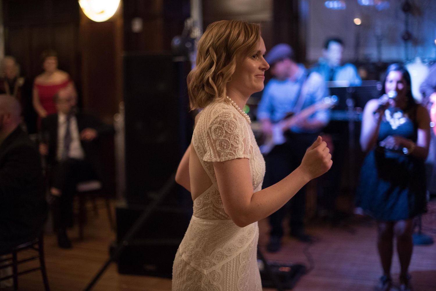 Bride in lace wedding dress dancing at reception with live band performing in background.