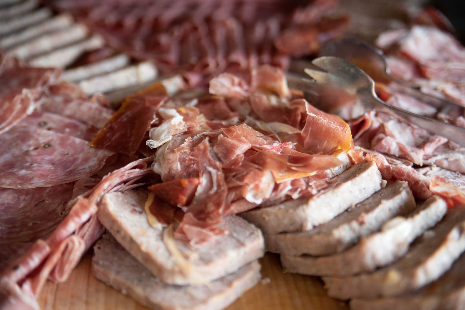 A charcuterie board with sliced prosciutto, salami, and bread arranged on a wooden cutting board.