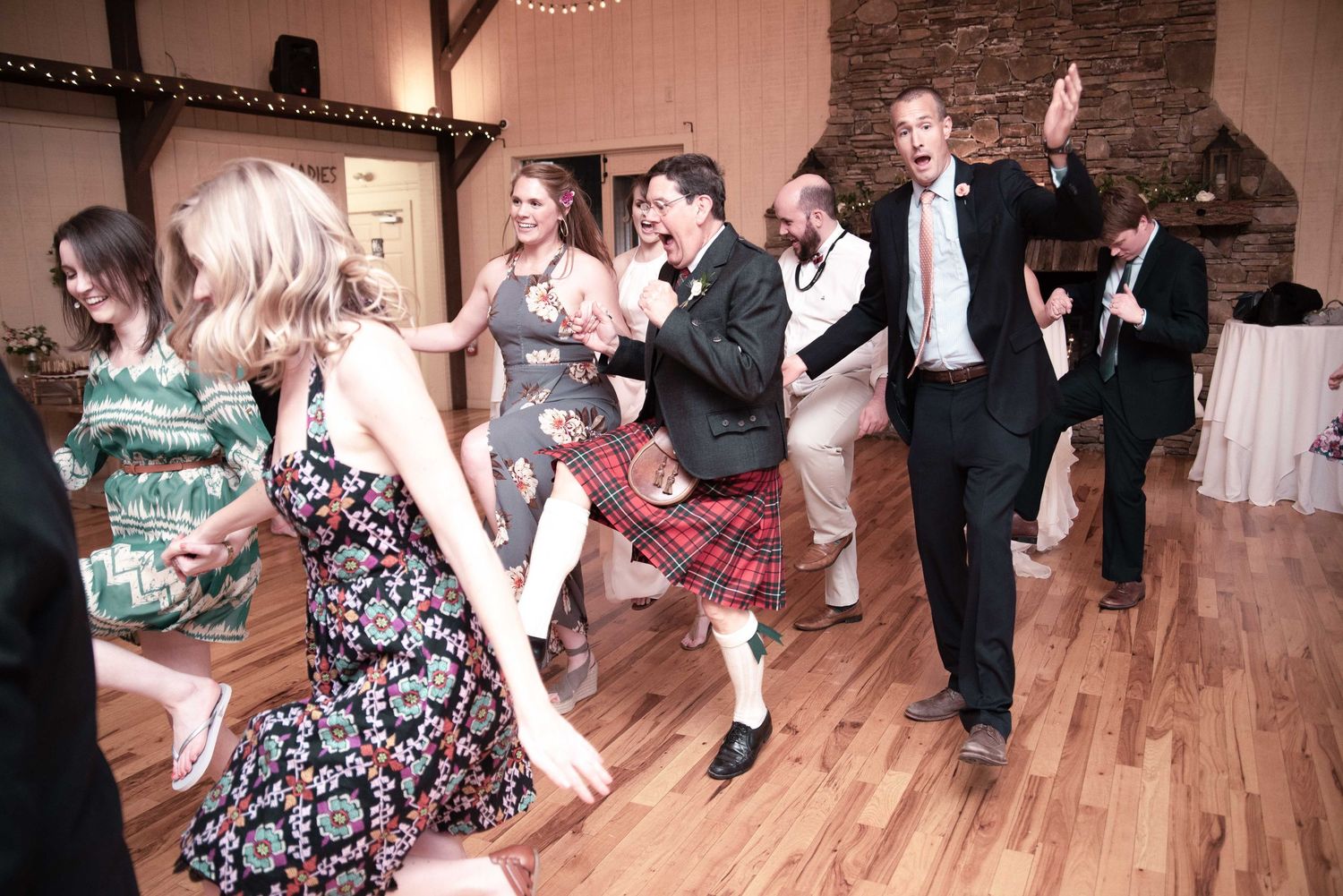 Guests dancing energetically at a wedding reception, with one man wearing a traditional Scottish kilt on the dance floor.