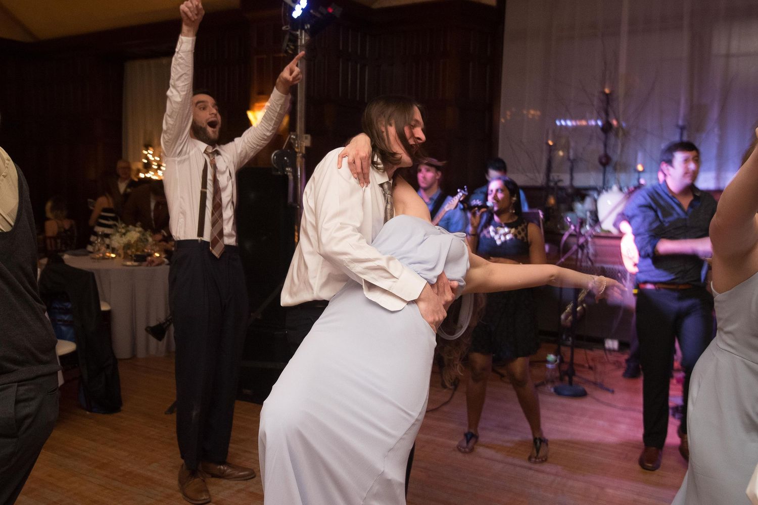 Couple sharing a romantic dip dance at a wedding reception with guests celebrating in the background.