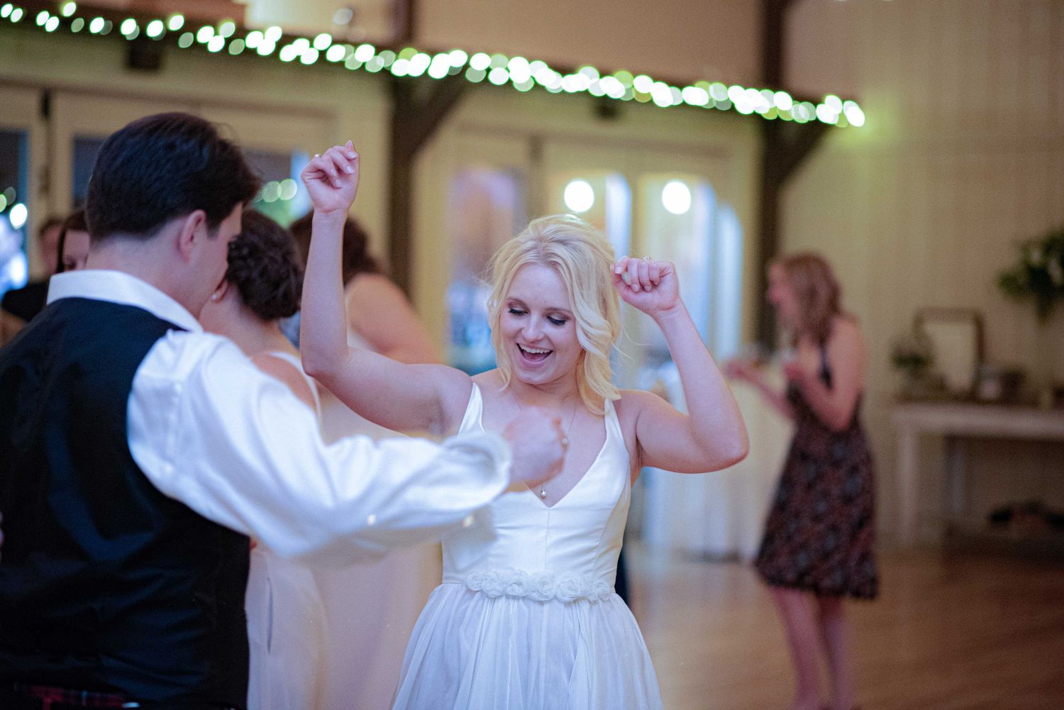 Bride in white wedding dress dancing joyfully with groom at elegant indoor wedding reception venue.