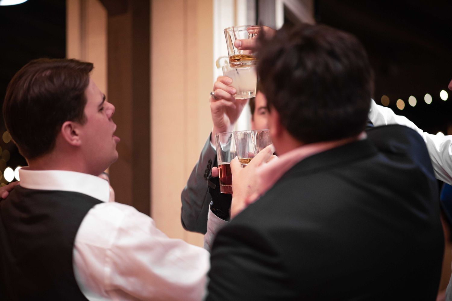 Three men in formal attire raising glasses in a celebratory toast at an evening event.