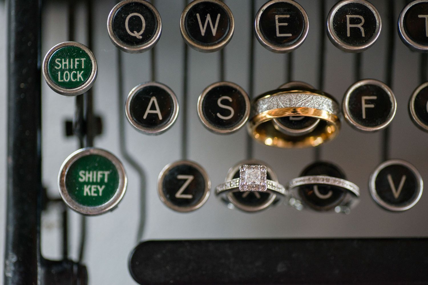 Wedding rings and gold band displayed on vintage typewriter keys for a creative detail shot.
