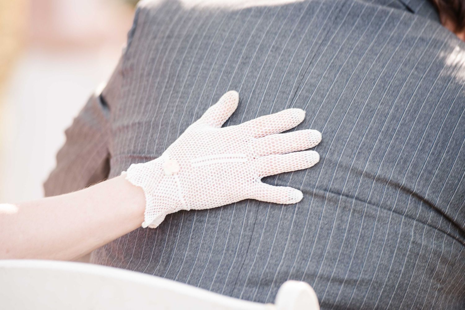 A white lace glove resting gently on a gray pinstripe suit jacket sleeve.