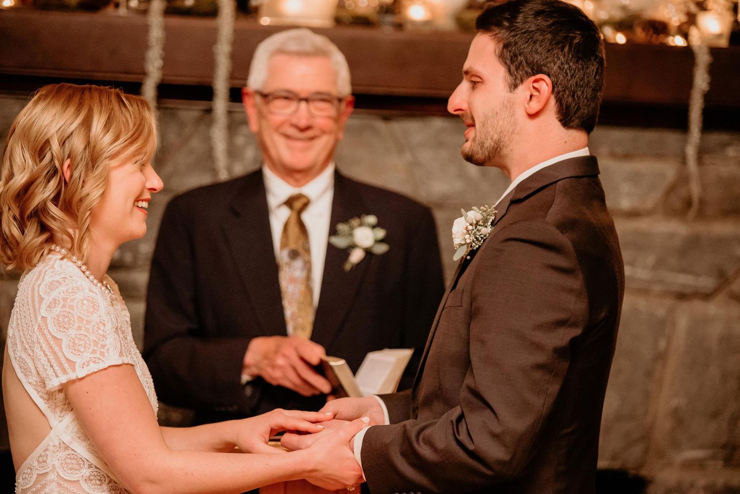Bride and groom exchange rings during intimate wedding ceremony with officiant at elegant candle-lit venue.