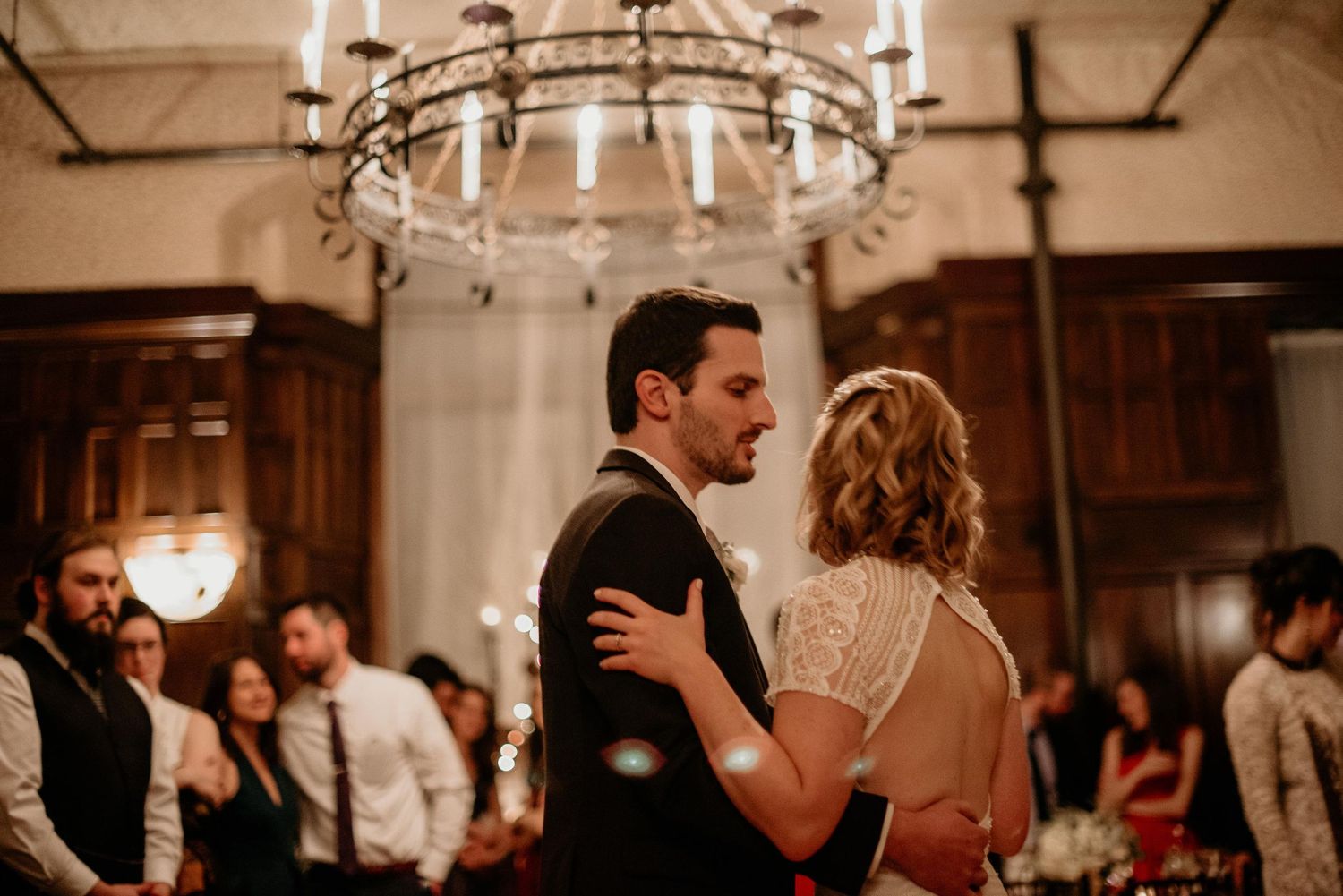 Bride and groom share their first dance under an elegant chandelier at a romantic wedding reception.