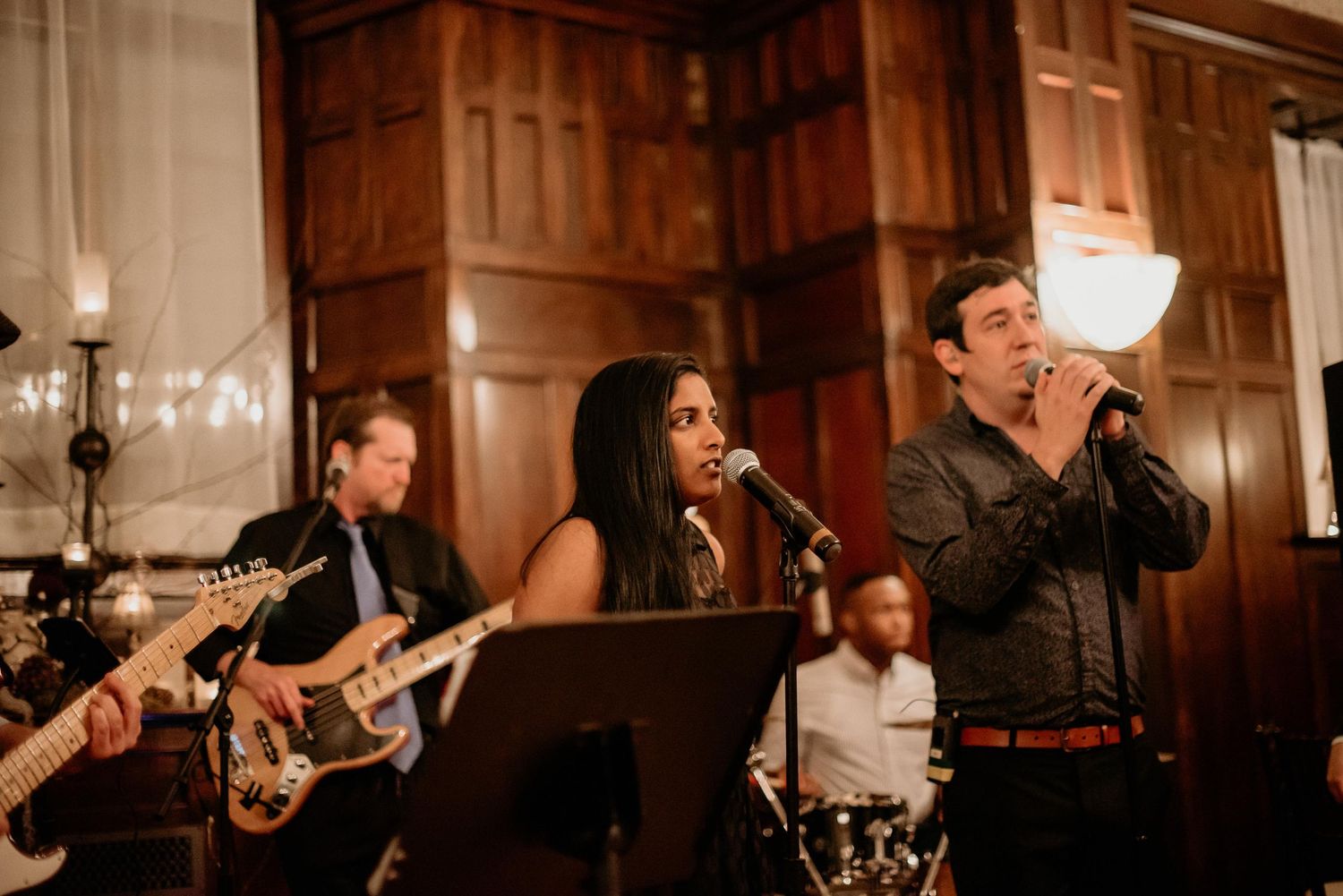 Live band performing at elegant wood-paneled venue, featuring female vocalist and male singer with microphone on stage.