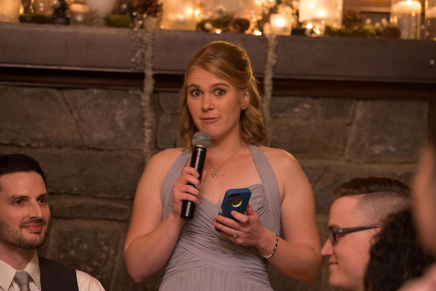 Bridesmaid in gray dress giving a speech with microphone at an elegant wedding reception.