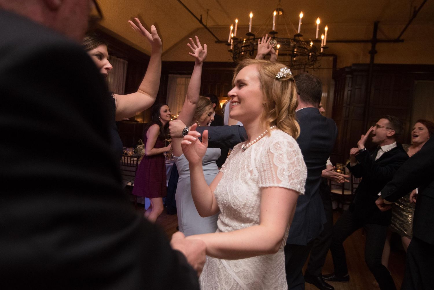 Bride dancing joyfully with guests at elegant wedding reception in candlelit venue.