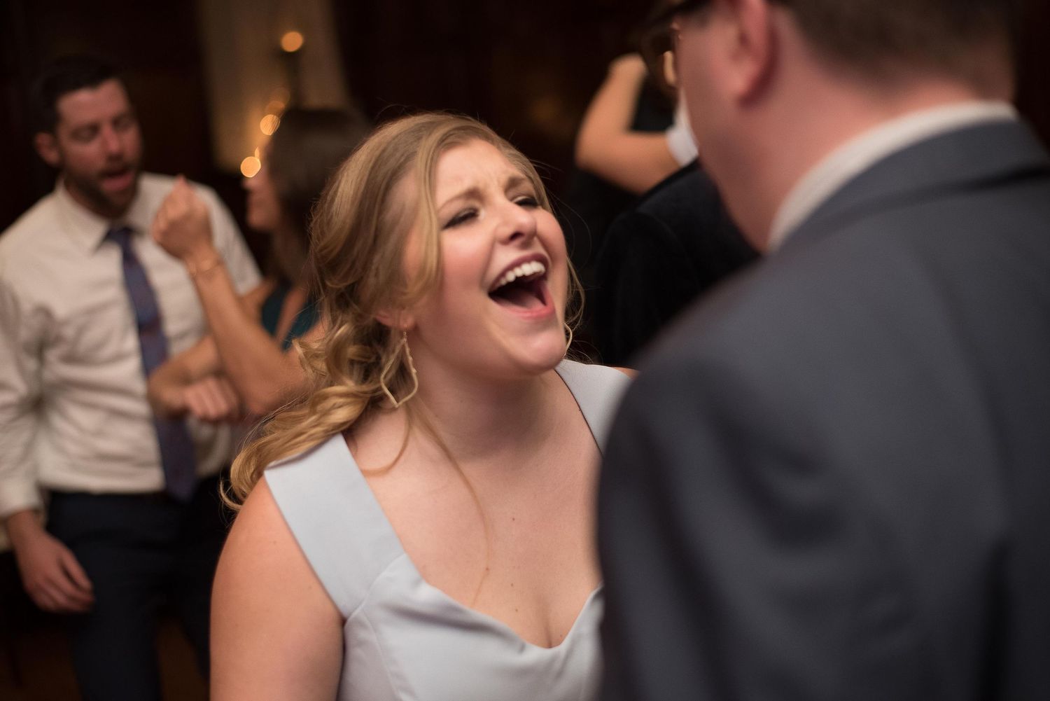 Bride laughing joyfully while dancing with guests at a wedding reception celebration.