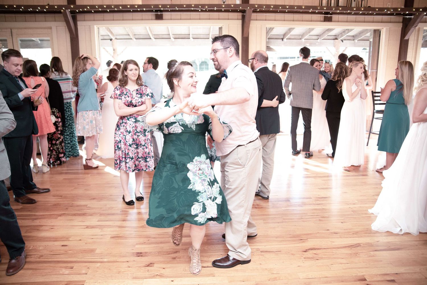 Guests dancing joyfully at a wedding reception in a rustic venue, with couples twirling on the dance floor.