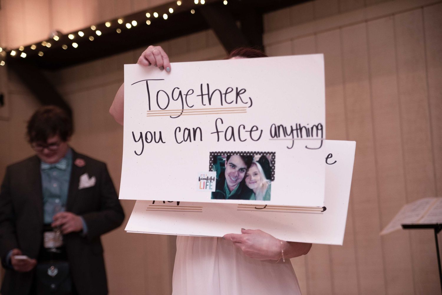 Bride holding a handmade wedding sign reading Together you can face anything with a couple photo at a reception.