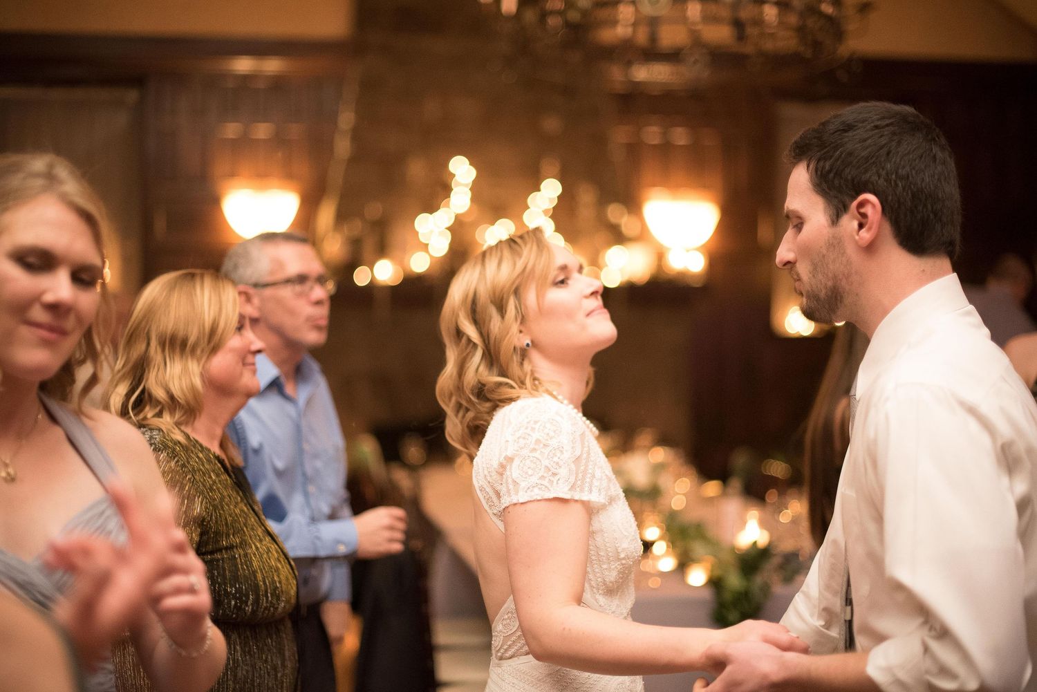 Bride and groom share a romantic first dance at elegant wedding reception with warm chandelier lighting.