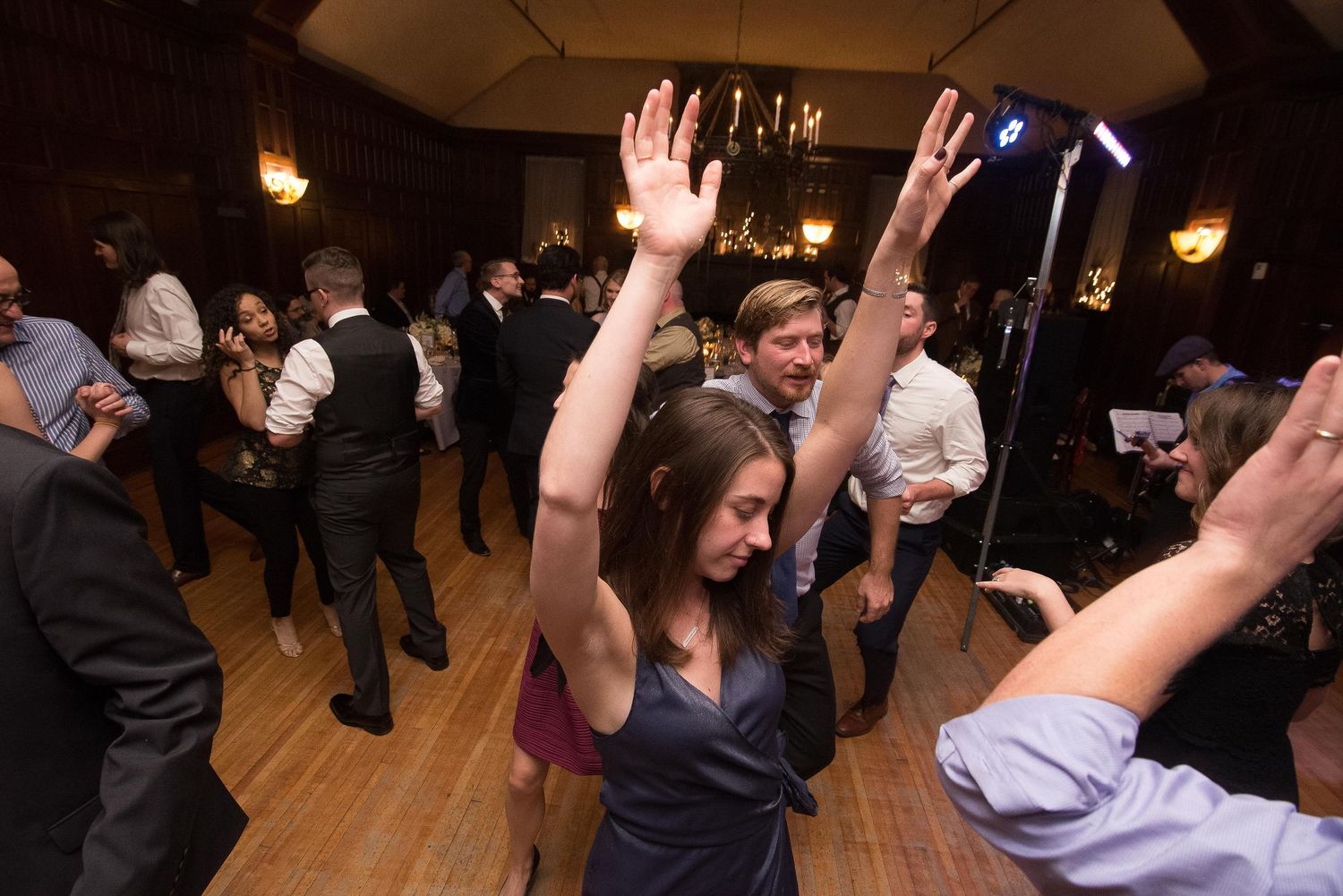 Guests dancing with hands raised at a lively indoor wedding reception in an elegant ballroom.