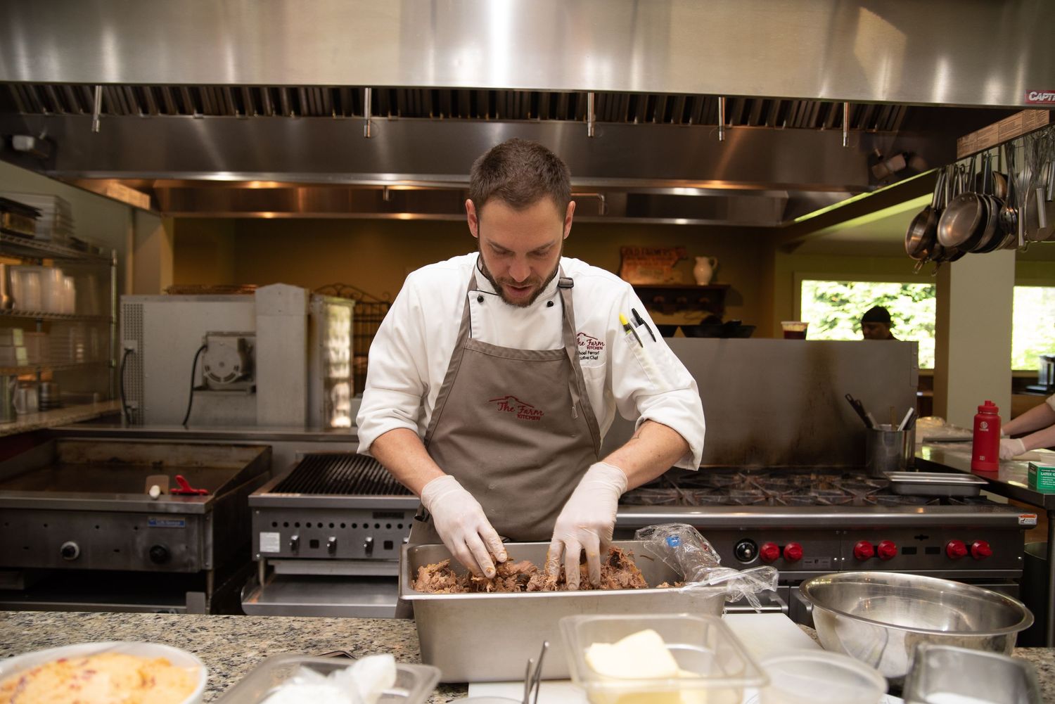 A chef in white coat and apron prepares food in a professional restaurant kitchen.