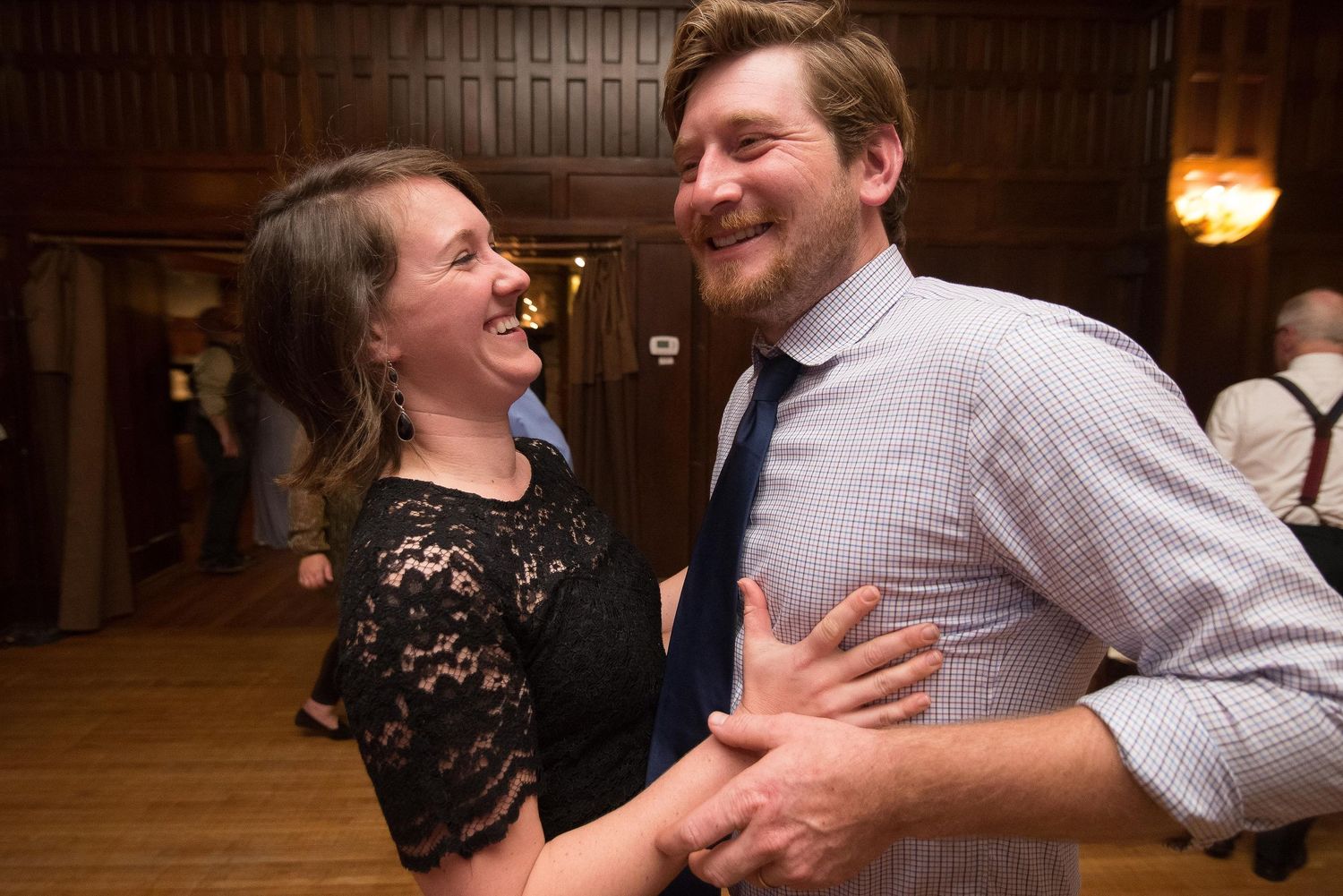 Couple laughing and dancing together at a formal indoor event, wearing elegant attire in a warmly lit venue.
