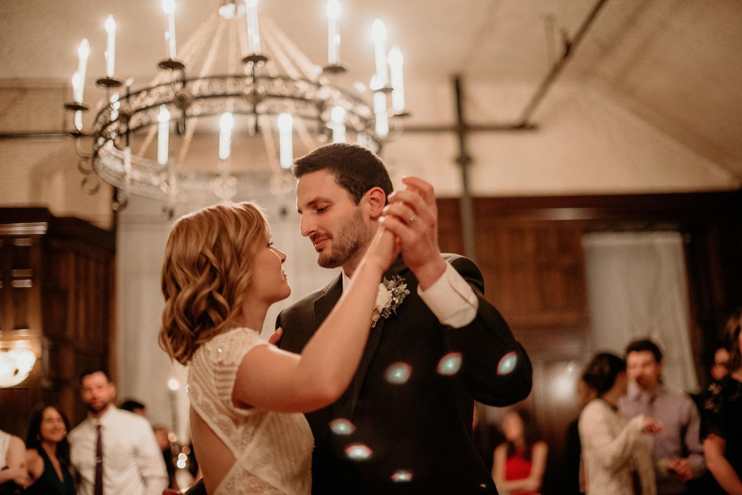 Bride and groom share their first dance under an elegant chandelier at a romantic wedding reception.