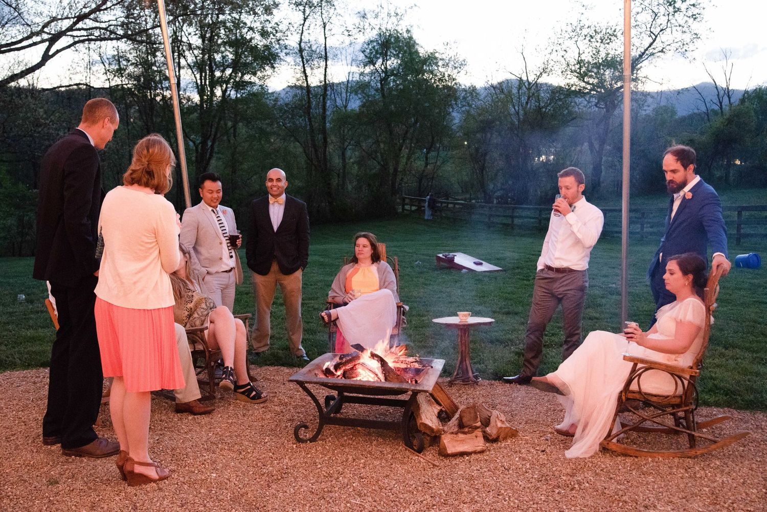 Group of people gathered around an outdoor fire pit at dusk during a backyard evening gathering.
