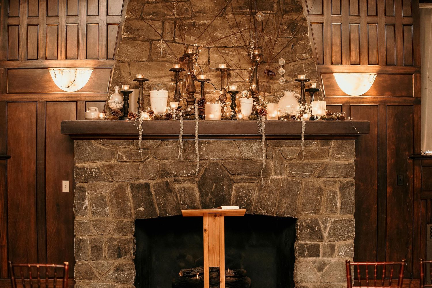 Rustic stone fireplace with candelabra mantel decor, wooden paneling, and warm ambient lighting in an elegant venue.