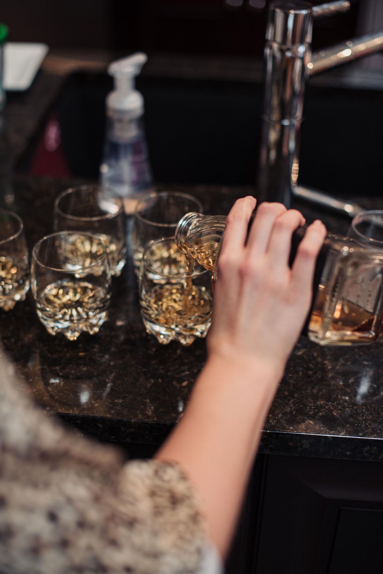 Bartender pouring whiskey into ornate crystal glasses on a dark granite bar counter.