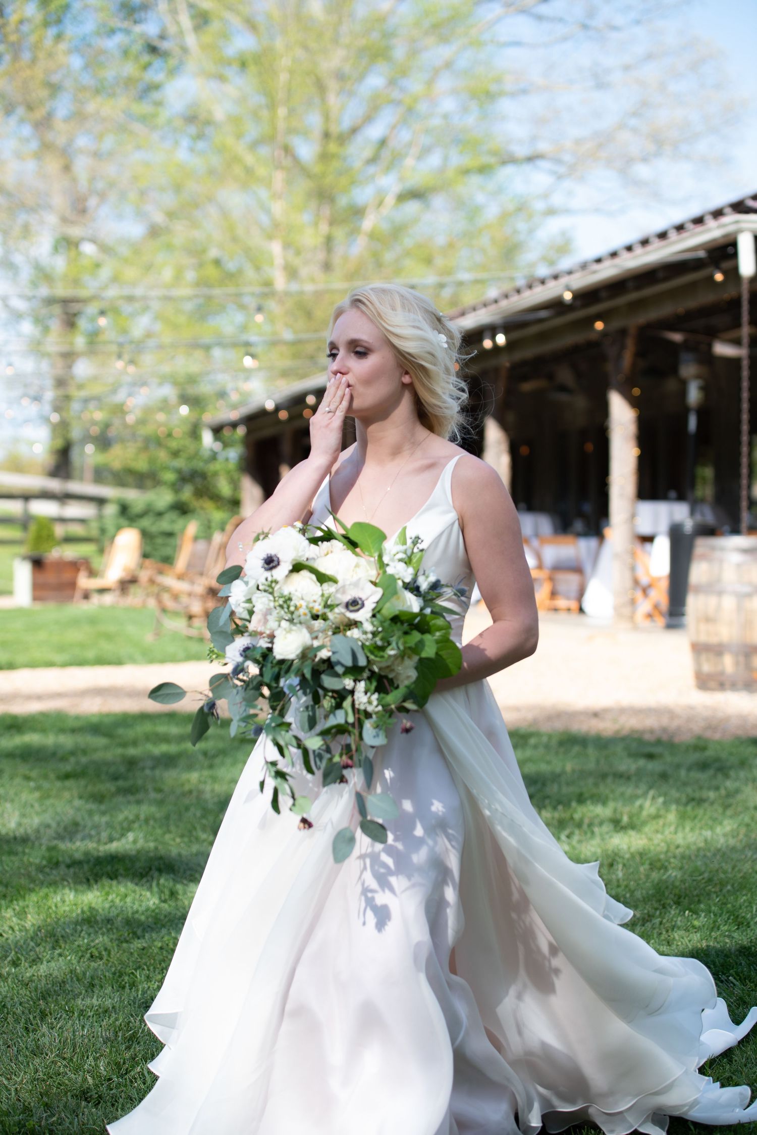 Blonde bride in white gown holding white floral bouquet on sunny wedding day.