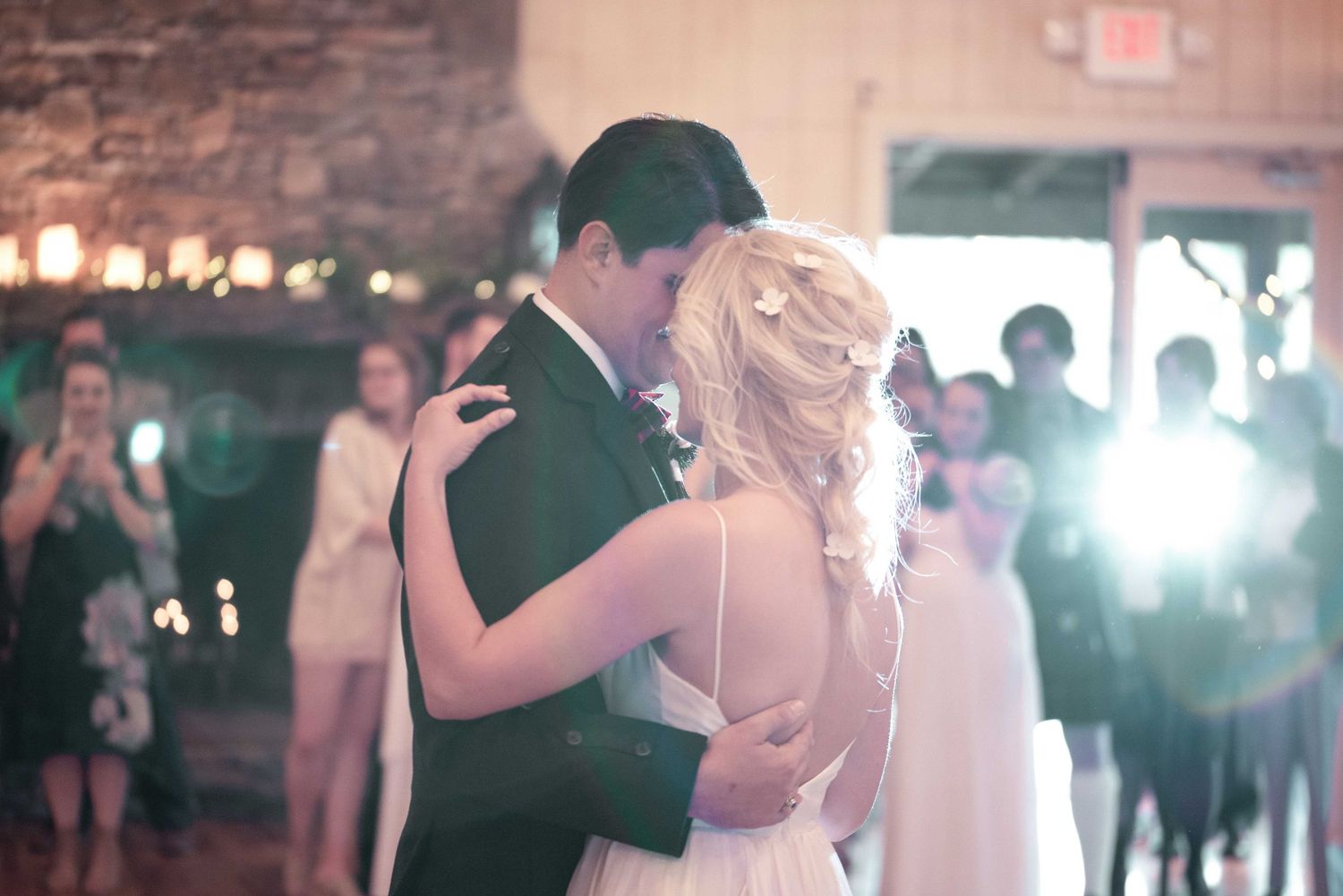 Bride and groom share their first dance at a romantic wedding reception with guests watching in the background.