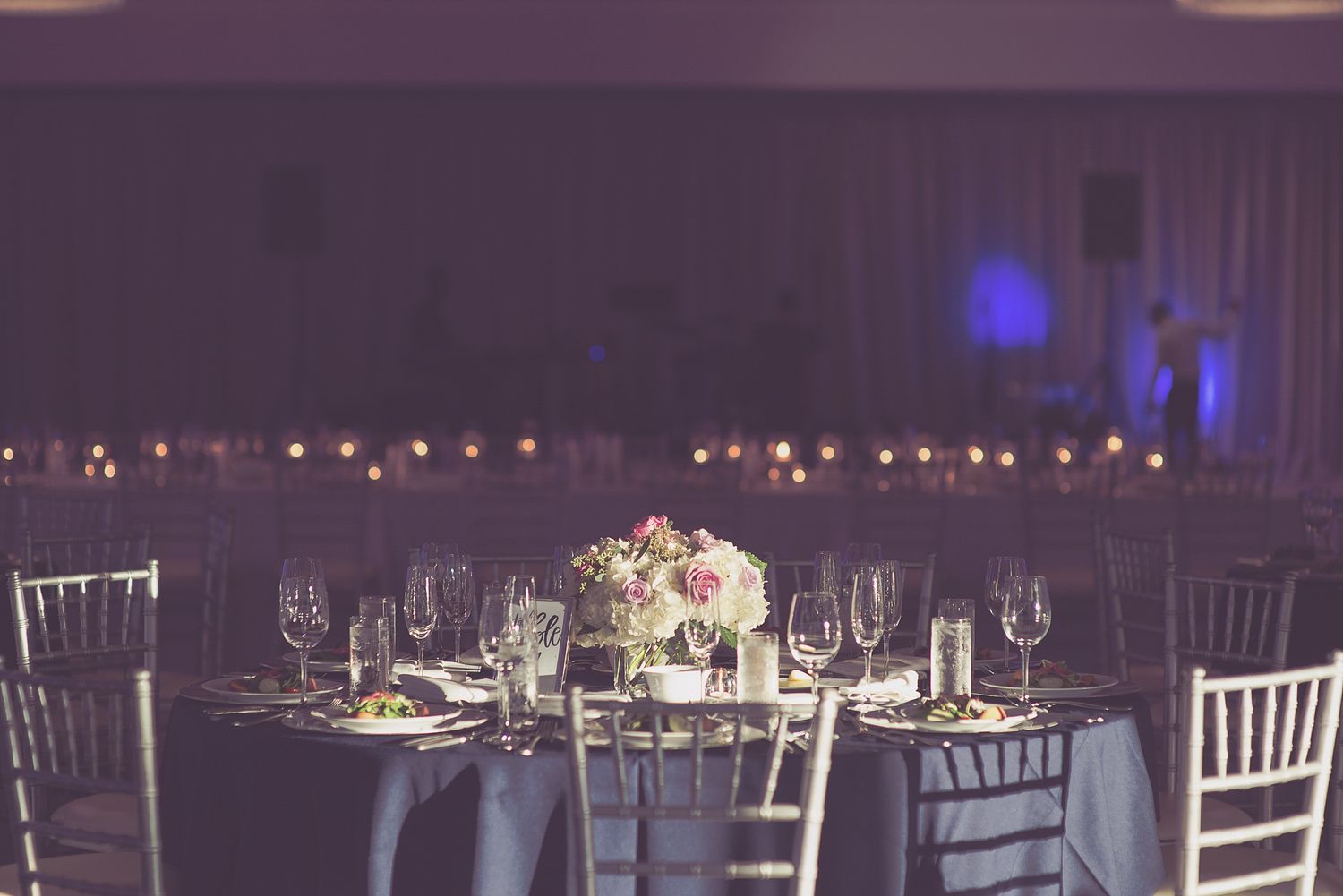 Elegant wedding reception table with floral centerpiece, crystal glasses, and warm string lights in background.