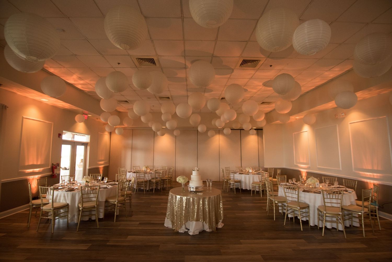 Elegant wedding reception hall decorated with white paper lanterns and warm amber uplighting.